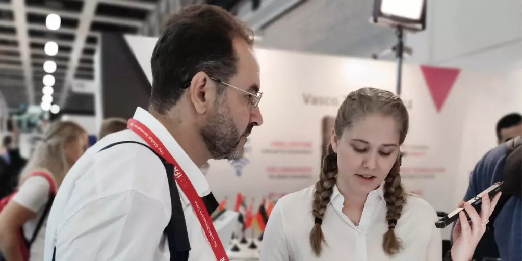 Une femme aux cheveux clairs tenant un Vasco Translator tout en parlant avec un homme à lunettes.