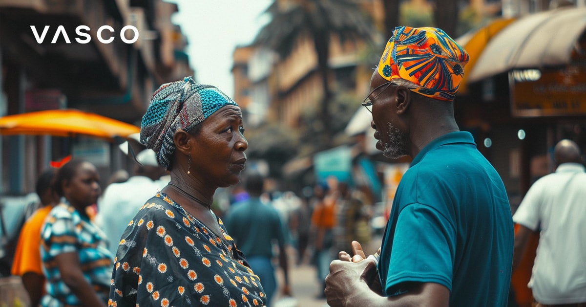 Un homme et une femme âgés conversant dans une rue animée avec des vêtements colorés et des personnes en arrière-plan.