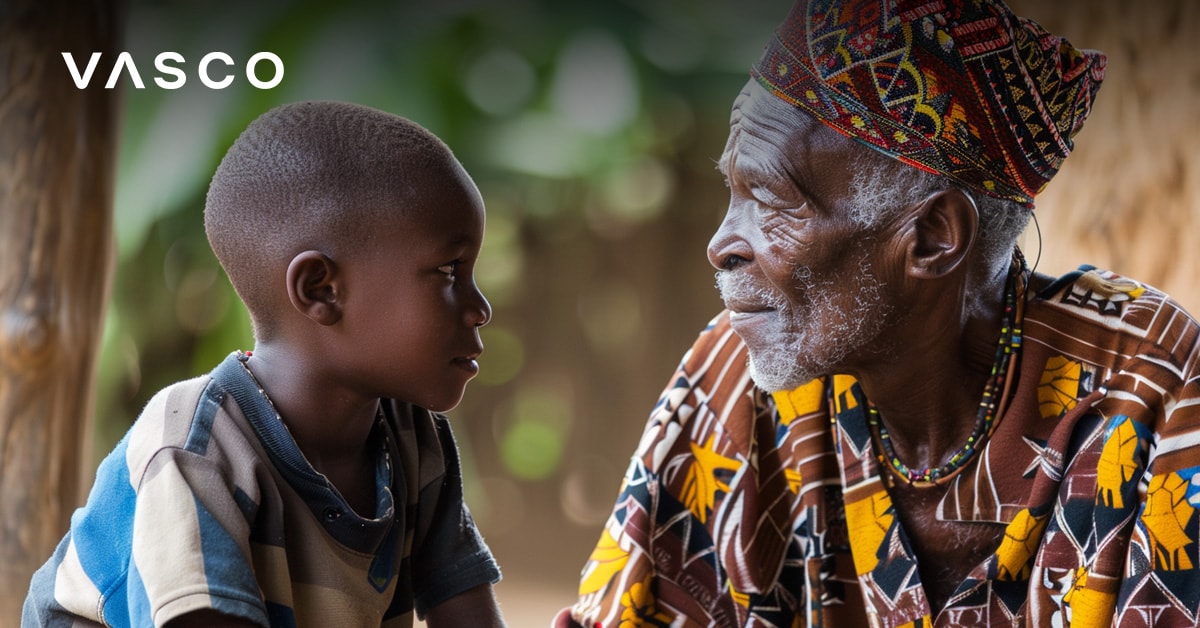 Un homme âgé en tenue traditionnelle colorée assis et parlant avec un jeune garçon, tous deux se regardant avec attention.