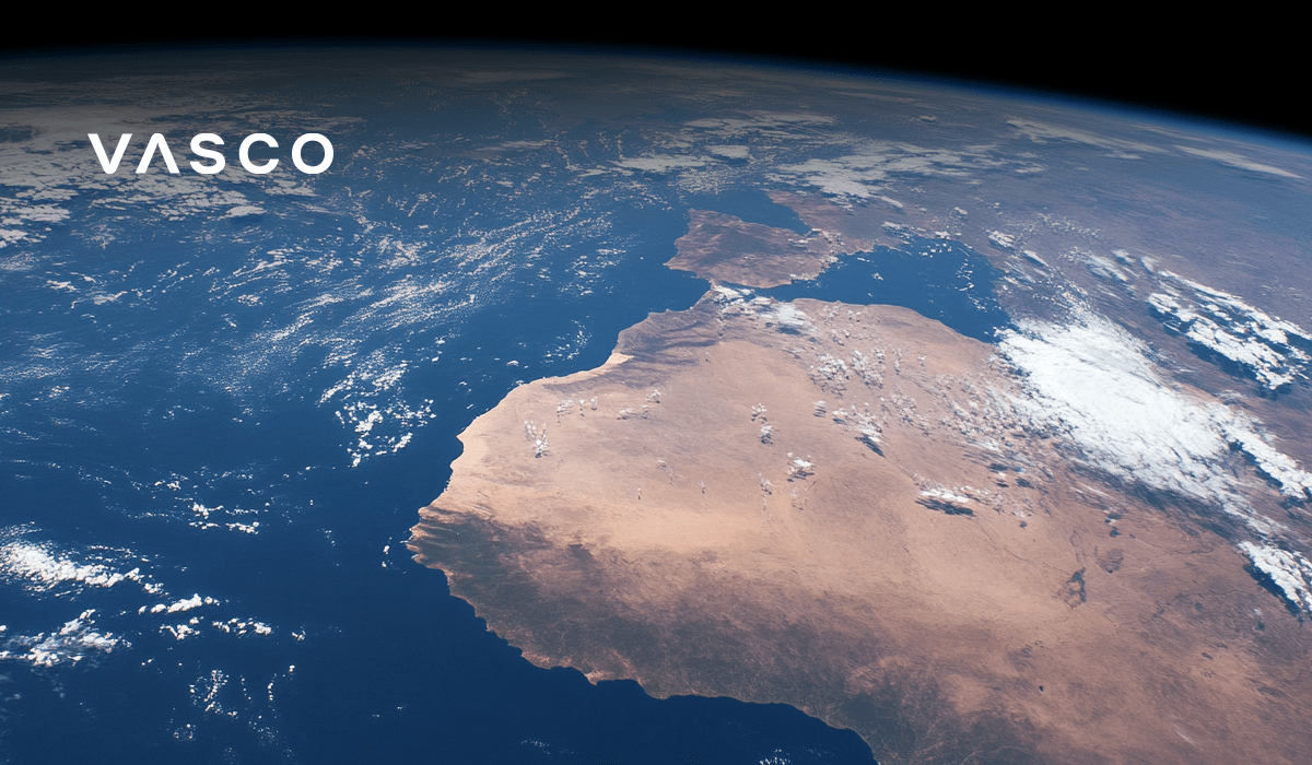 Vue de la Terre depuis l'espace, montrant un vaste paysage désertique bordé par l'océan, avec des nuages épars au-dessus.