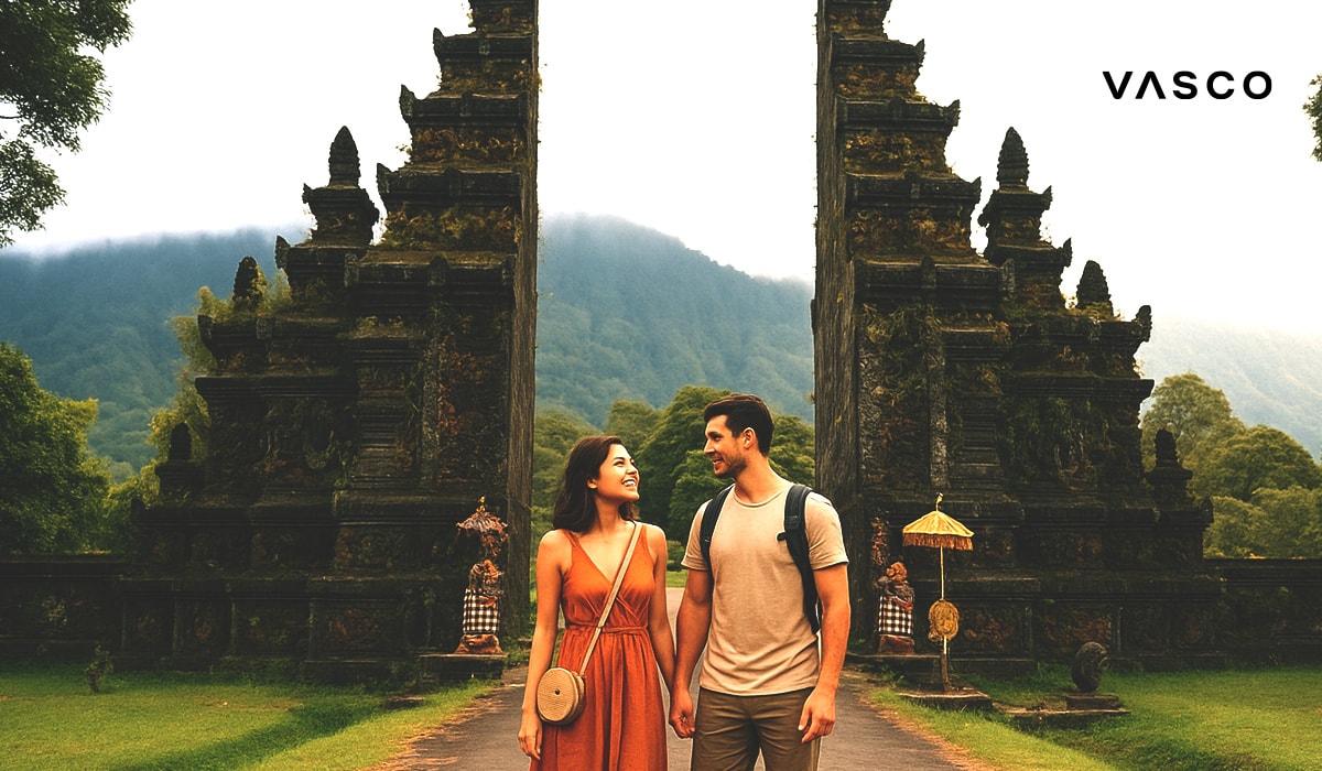 Un couple se tenant par la main devant une porte de temple balinais (candi bentar), avec les montagnes verdoyantes en toile de fond.
