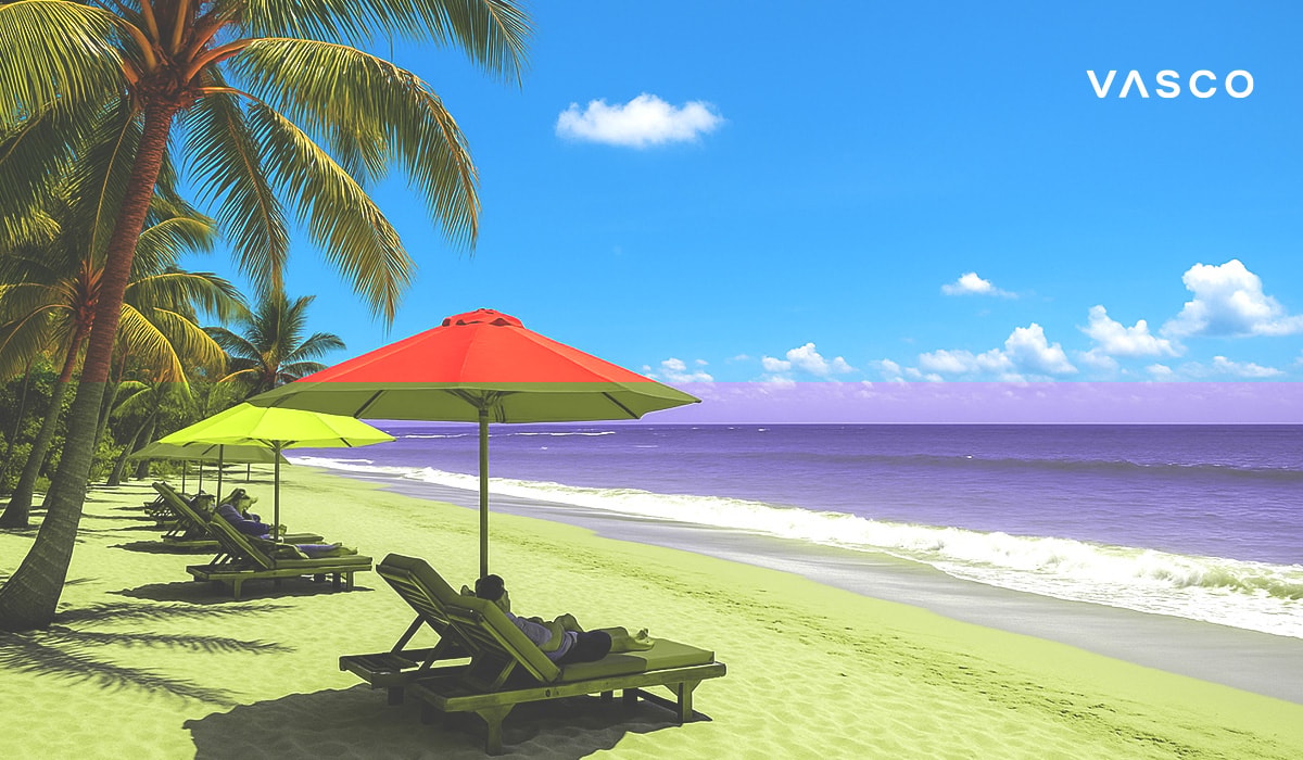 Des touristes se détendent sur des transats à l’ombre de parasols rouges et jaunes, sur une magnifique plage de sable bordée d’une eau turquoise.