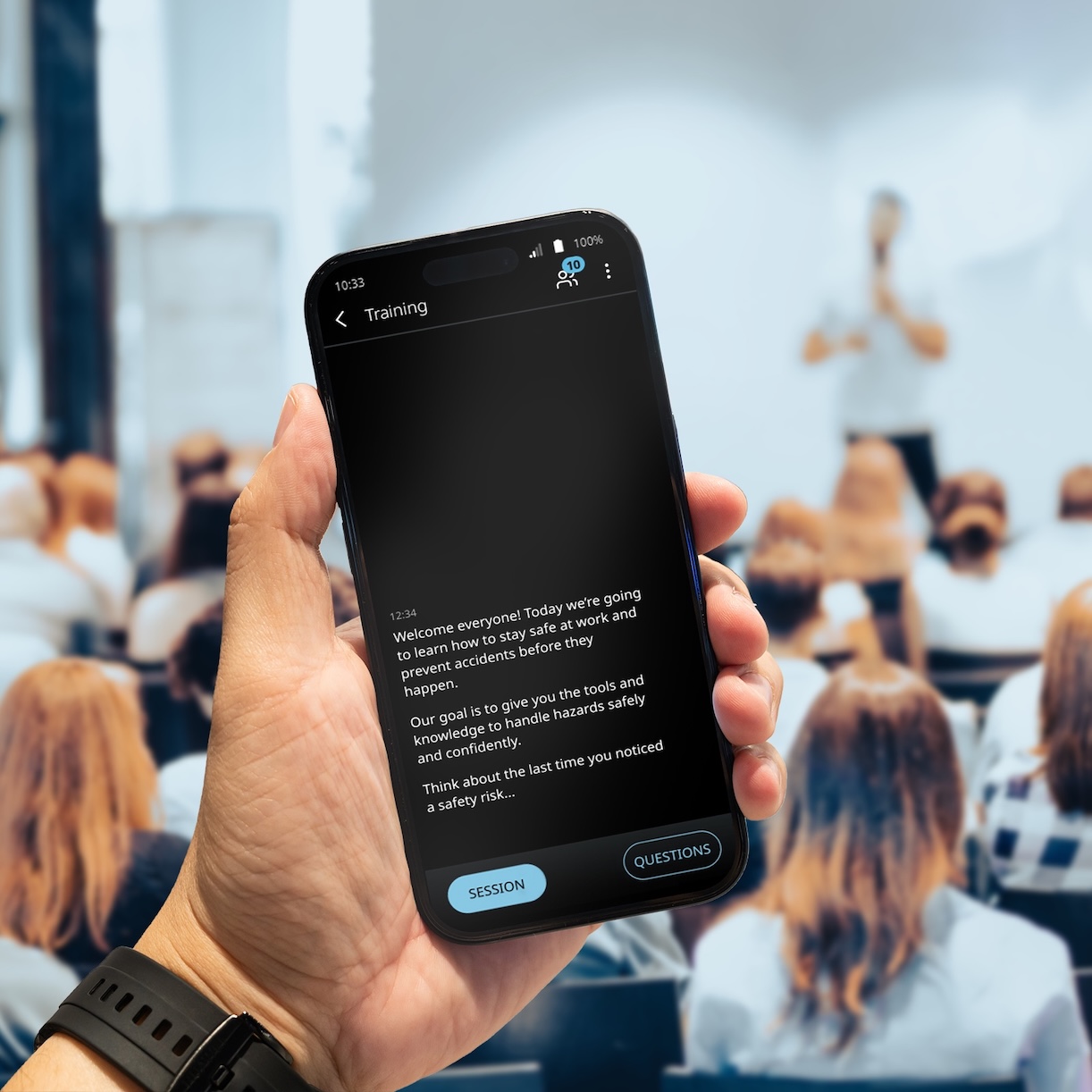 Vasco Audience Une conférence se déroule dans une salle bondée. Un homme tient dans sa main un téléphone sur lequel s'affiche la traduction grâce à Vasco Audience