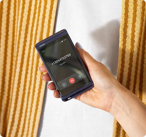 Une personne tenant le Vasco Translator Q1. L'écran affiche la fonction d'appel avec un numéro de téléphone, l'état « En cours d'appel » et le mode conversation.