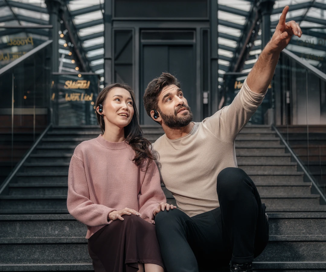 Couple sitting on the stairs and communicating with translating headphones. Man points at something in the distance.