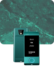 Une image de présentation du produit montrant un appareil Vasco Translator de couleur turquoise sous deux angles différents, sur un fond de tissu sombre et texturé. L'appareil de gauche présente une vue arrière, mettant en évidence l'objectif de l'appareil photo avec son flash et le logo « VA » en relief. L'appareil de droite présente une vue de face avec son écran allumé, affichant les messages « Hello ! », « VA », « ¡Hola ! » et le logo « VASCO Translator ». Un bouton circulaire situé au bas de la face avant de l'appareil est souligné d'une lumière bleue brillante. L'arrière-plan présente un motif de marbre vert luxueux avec des veines de couleur claire.