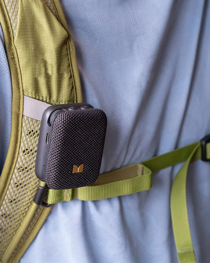 Mini-enceinte Bluetooth noire accrochée à la sangle vert olive d'un sac à dos